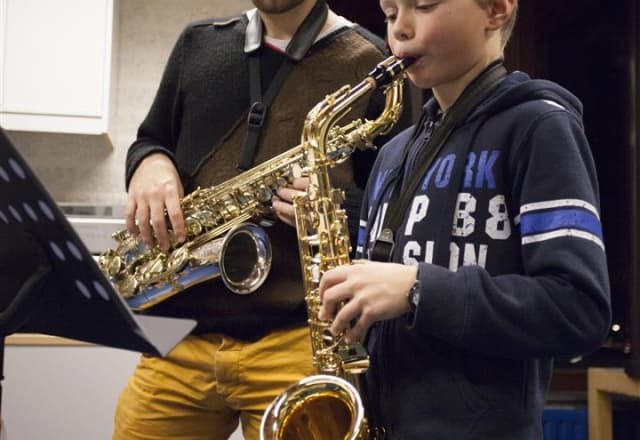Saxofoon, docent kijkt naar kind die aan het spelen is