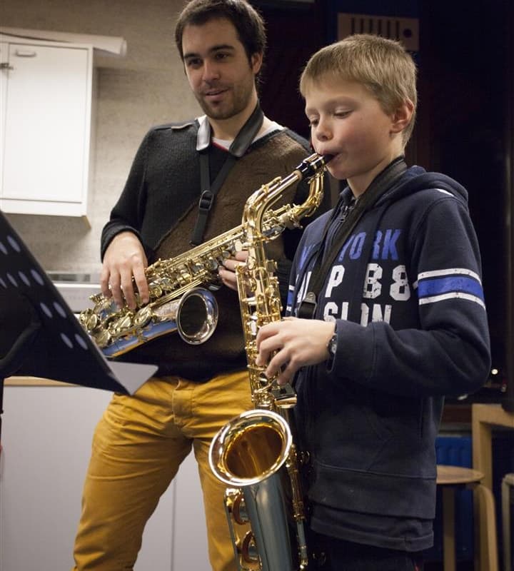 Saxofoon, docent kijkt naar kind die aan het spelen is